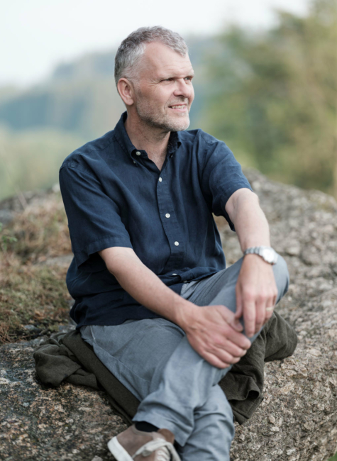 Reinhard Honeder sitzt locker auf einem großen Granitstein inmitten der Mühlviertler Landschaft.